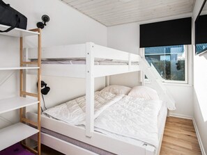 A bunk bed with a wooden ladder, a white wall, and a window with a view of the outside.