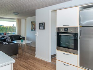 A modern kitchen with a built-in oven and refrigerator, a dining area with a table and chairs, and a living area with a sofa and a painting on the wall.