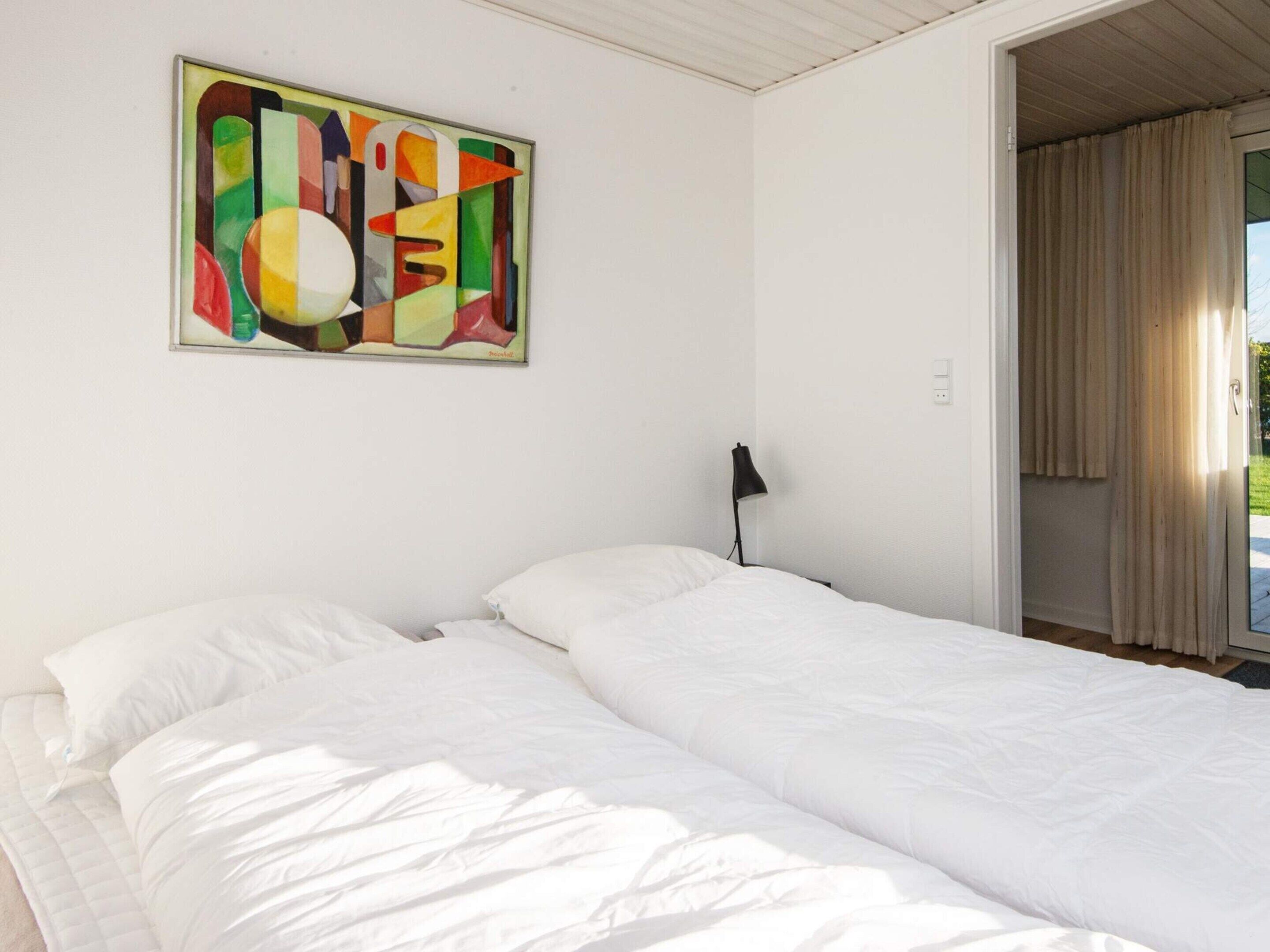 A hotel room with a bed, a painting on the wall, and a window with curtains.