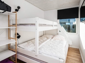 A bunk bed with a wooden ladder, a white wall, a window with a view, and a black object on the wall.