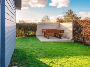 A wooden bench in a grassy backyard with a wooden fence and trees in the background.