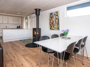 Una cocina moderna con estufa de leña, zona de comedor con mesa y sillas blancas, y un cuadro abstracto colorido en la pared.