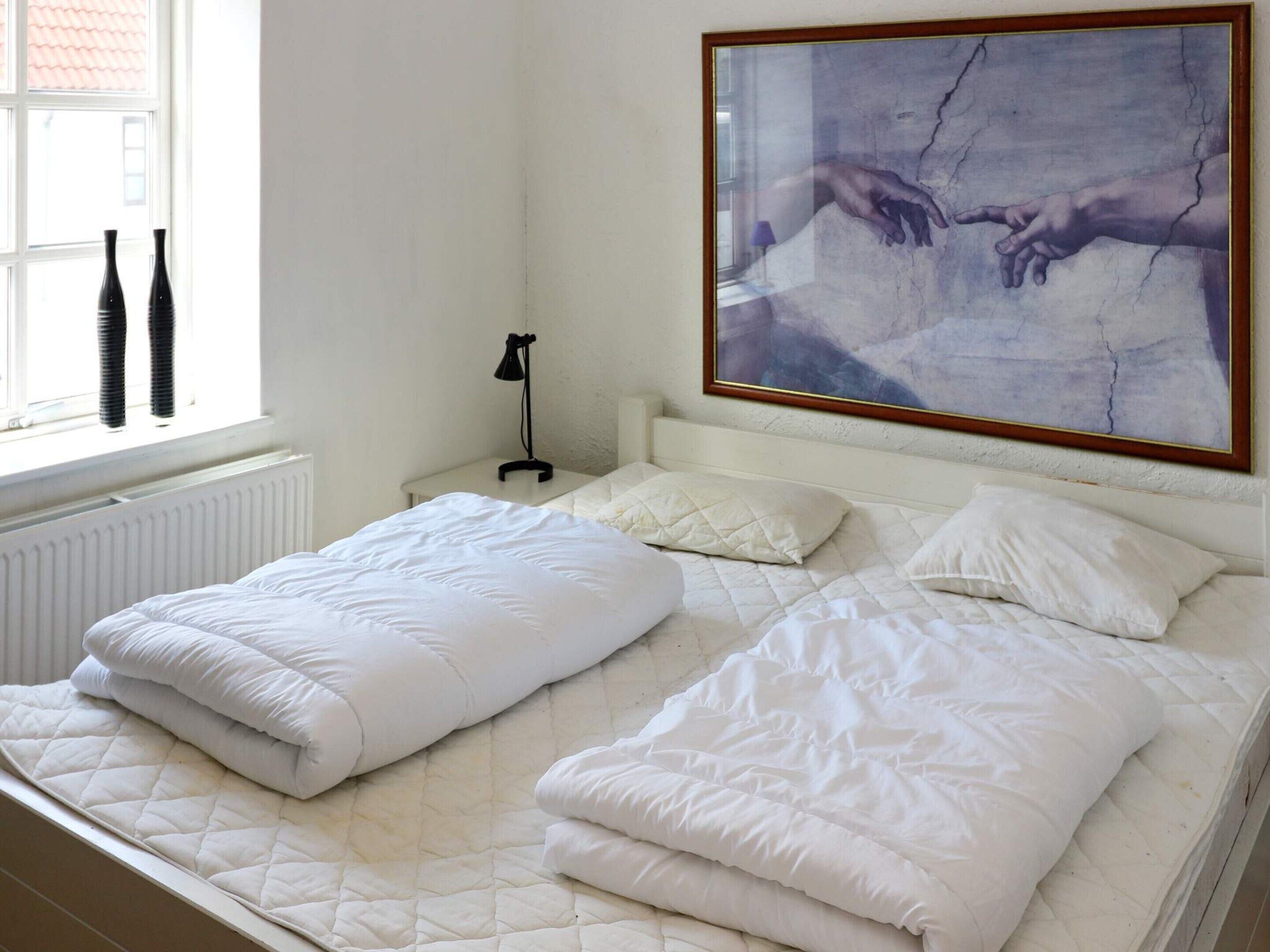 A neatly made bed with white bedding, a bedside lamp, and a framed artwork above it.