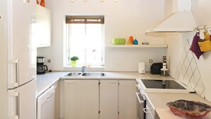 A compact kitchen with white cabinets, a double sink, a coffee maker, and a window with blinds. - 8 Person Holiday Home in Storvorde (Storvorde)