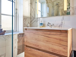 A bathroom with a marble backsplash, a wooden vanity, a mirror, and a shower area. - 4 Person Holiday Home in Nexo (Nexø)