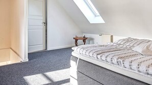 A bedroom with a sloped ceiling, a skylight, a bed with patterned bedding, a small wooden table, and a radiator. - 4 Person Holiday Home in Nexo (Nexø)