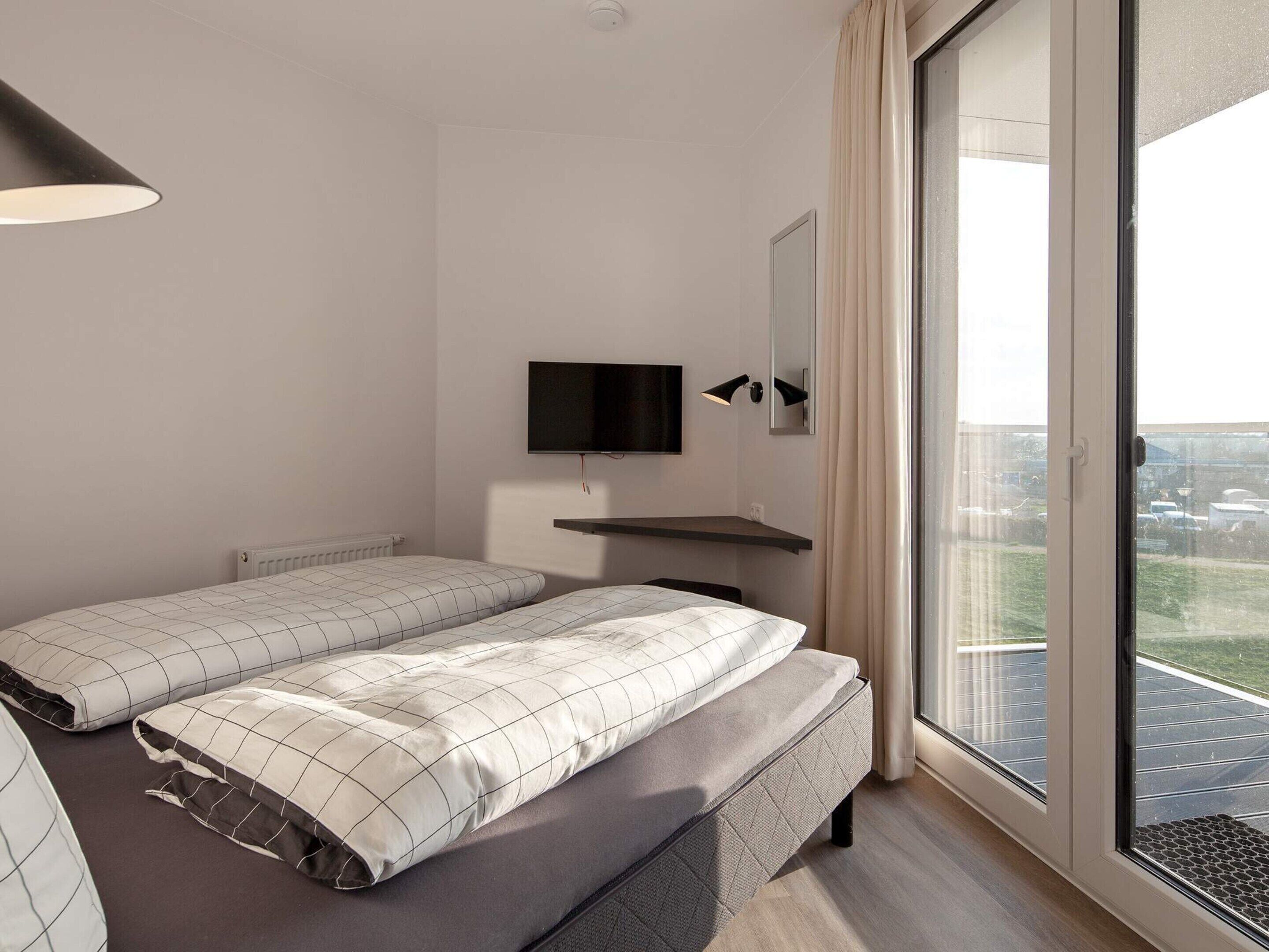 Une chambre moderne avec deux lits, une télévision, un miroir et une grande fenêtre donnant sur un beau paysage.