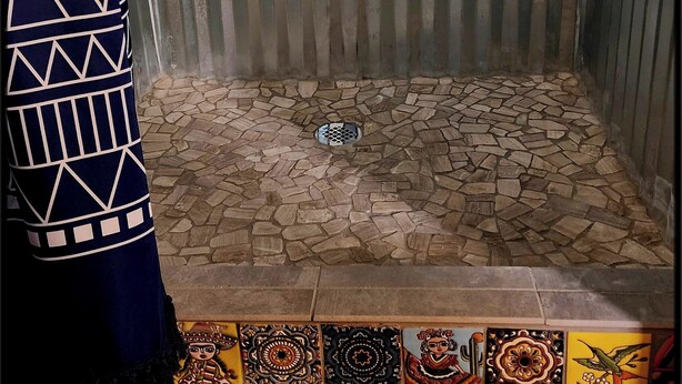 A shower with a metal door, a drain, and a patterned floor. - The Artists Cottage ~ Fun desert getaway (Ajo)