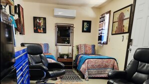 A room with two black leather chairs, a bed with patterned bedding, a blue storage unit, and a large decorative rug. - The Artists Cottage ~ Fun desert getaway (Ajo)