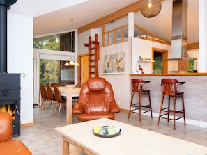 Un vaste espace de vie comprenant un coin salon avec cheminée, une table à manger et une cuisine ouverte avec un bar.