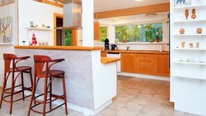 A modern kitchen with wooden cabinets, a central island, bar stools, and a window with a view of greenery.