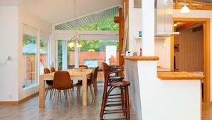 A spacious dining area with a wooden table and chairs, a hanging light fixture, and a view of the outdoors.