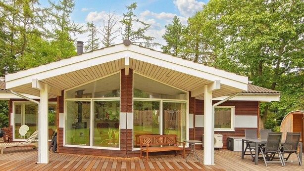 A modern house with a wooden deck, large glass windows, and a covered patio area.