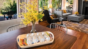 Et spiseområde med et træbord, en vase med gule blomster og en bakke med vand på flaske og snacks.