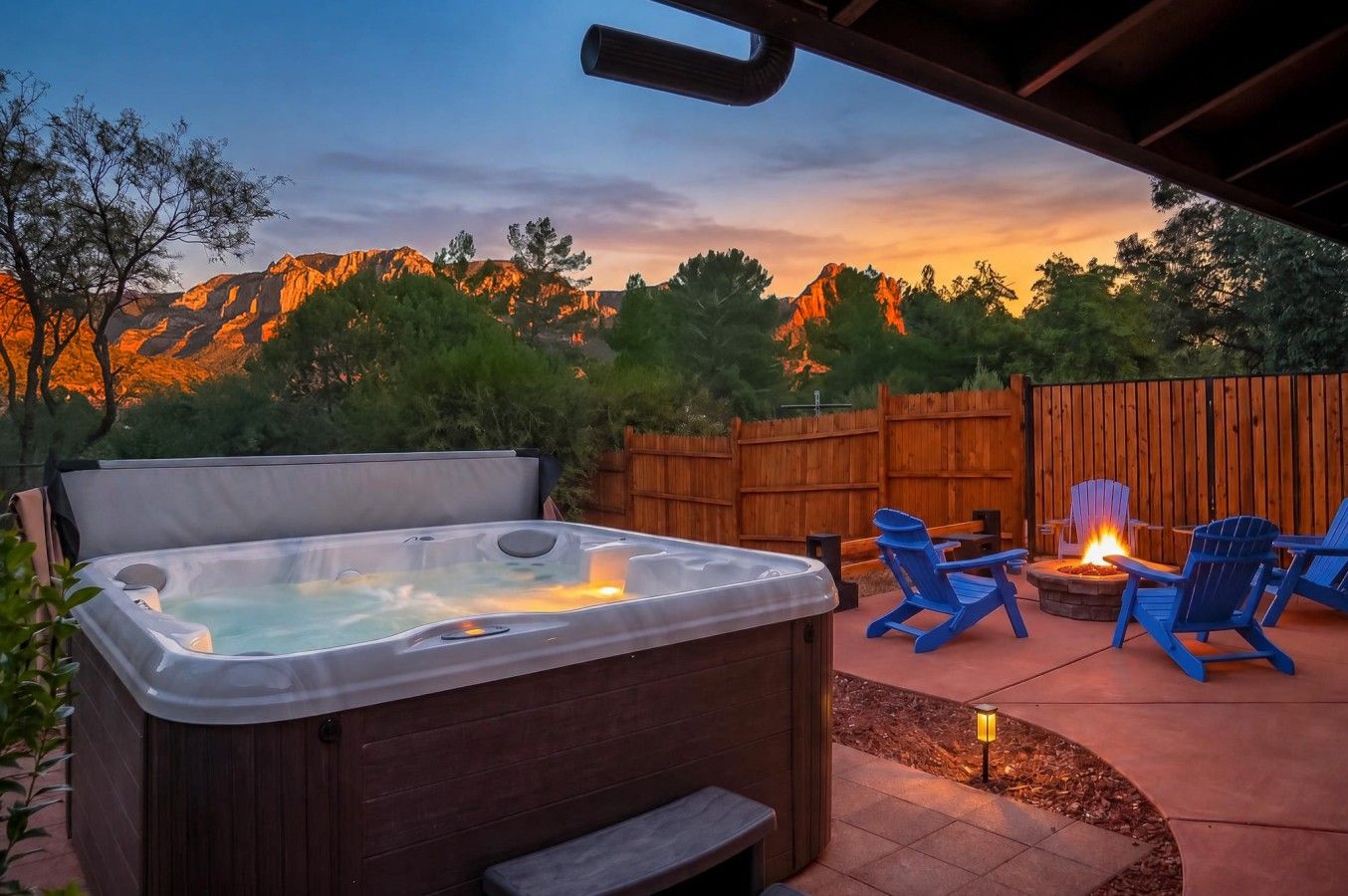 Un espace extérieur aménagé avec un jacuzzi, une terrasse en bois, des chaises bleues et un foyer.