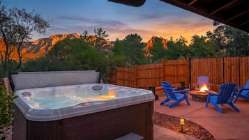 Un espace extérieur aménagé avec un jacuzzi, une terrasse en bois, des chaises bleues et un foyer.