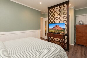 Une chambre d’hôtel avec un lit, un téléviseur posé sur un meuble en bois, une commode et un mur orné d’un motif géométrique.