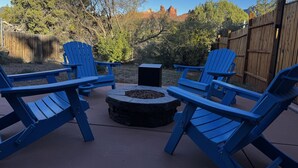 Un patio con cuatro sillas Adirondack azules dispuestas alrededor de un hogar de piedra.