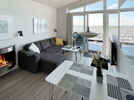 Una sala de estar moderna con chimenea, un sofá, una mesa de comedor y grandes ventanas con vistas a la ciudad.