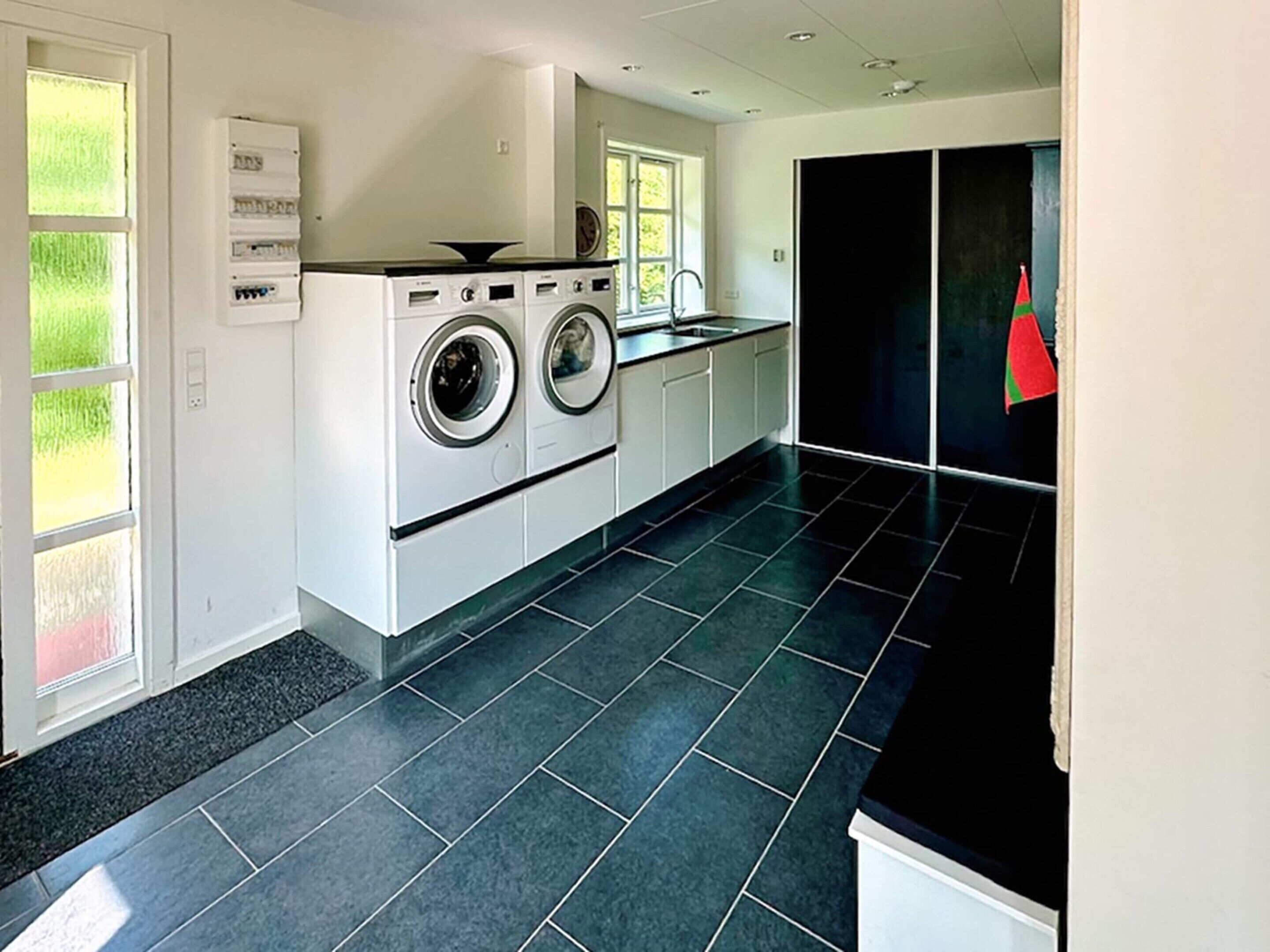 A modern laundry room with a washing machine and dryer, a sink, and a large window.