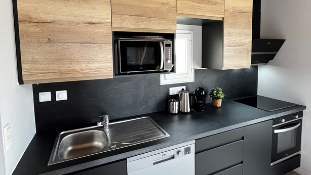 A modern kitchen with wooden cabinets, a black countertop, a built-in microwave, a sink, and a dishwasher.