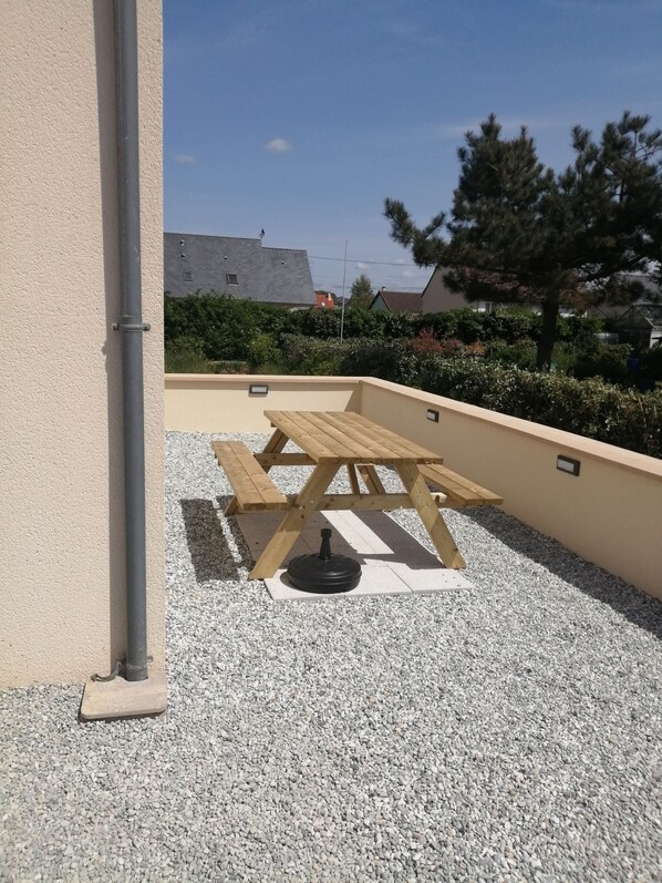 A rooftop patio with a wooden table and a weight bench.