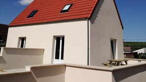 A two-story building with a red-tiled roof, two small windows, and a white exterior wall.