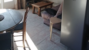 A compact living space with a wooden ceiling, a round mirror, a television, a refrigerator, a dining table with chairs, and a sofa.