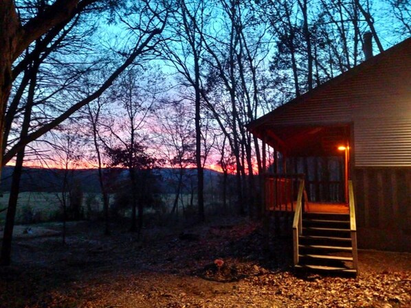 A cabin with a wooden exterior, a staircase leading to the entrance, and a view of the surrounding forest.