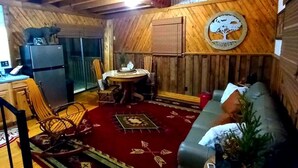 Interior acolhedor de cabana com teto de madeira, sala de jantar com mesa e cadeiras, sofá e ventilador de teto.