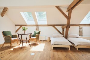 Una habitación con techo inclinado, vigas de madera, dos camas, una mesa con sillas y una ventana.
