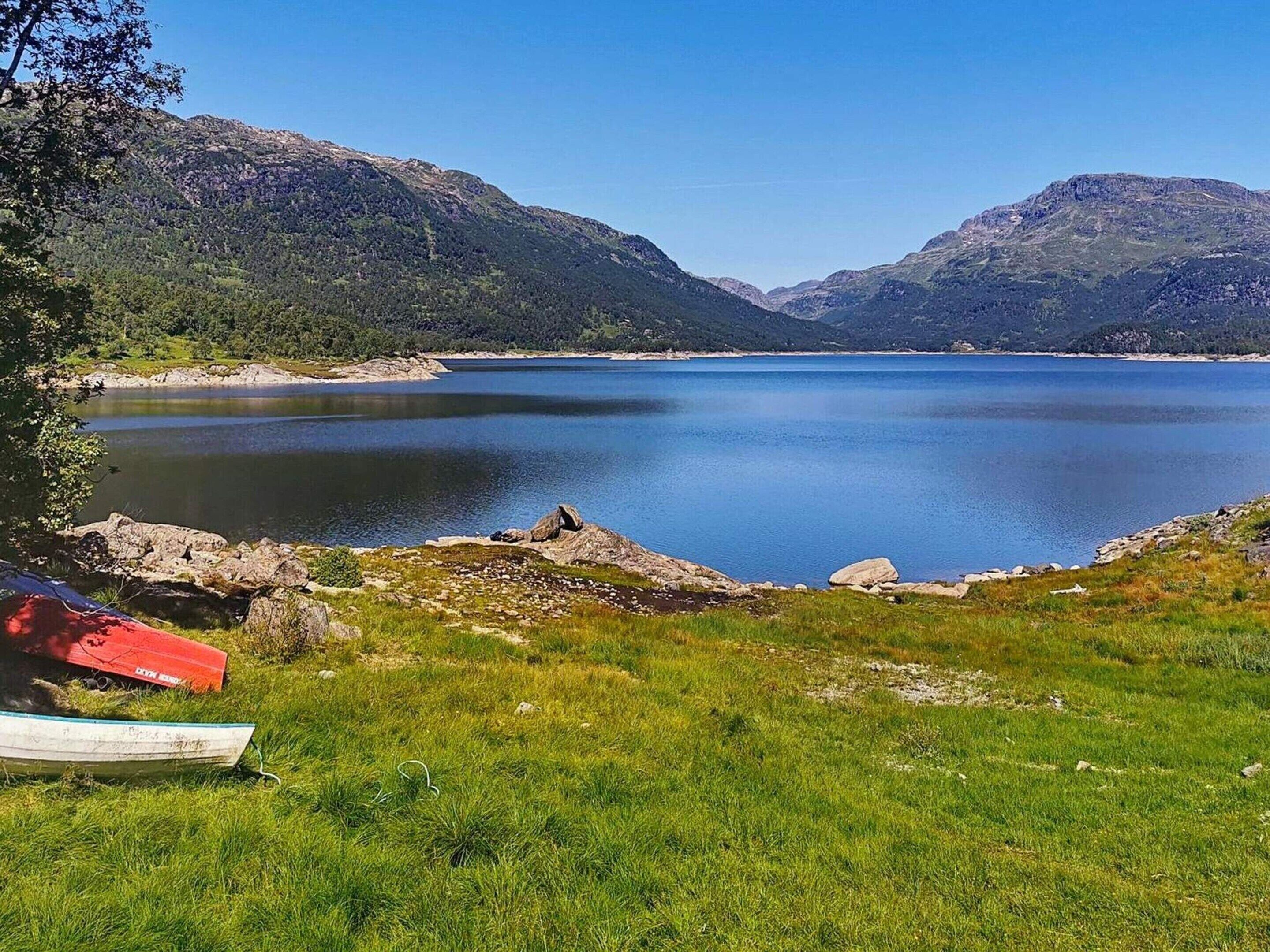 A serene lake surrounded by mountains, with a grassy area and a red tent in the foreground.