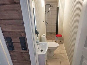 A narrow bathroom with a white sink, toilet, and shower area.