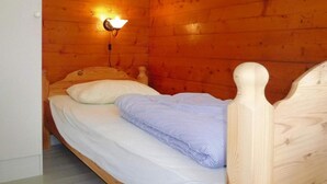 A wooden cabin room with a single bed, a wall-mounted light, and a wooden headboard.