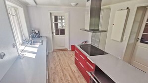 A modern kitchen with a long countertop, a stainless steel range hood, and wooden flooring.