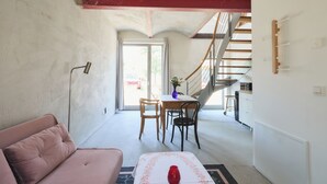A living room with a sofa, a dining table with chairs, a vase, and a staircase leading to an upper floor.