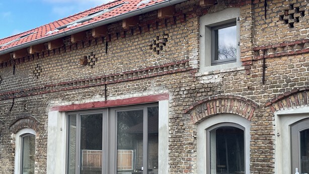 A building with a brick facade, large glass doors, and a red-tiled roof.