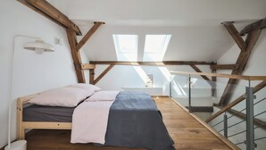 A loft bedroom with a wooden bed, skylights, and a glass railing staircase.