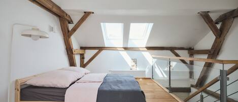 A loft bedroom with a wooden bed, skylights, and a glass railing staircase.