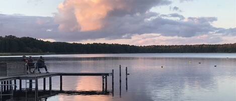 A calm lake with a wooden dock and a few people sitting on it.