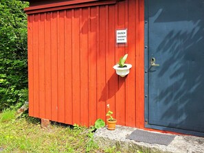 A red shed with a door, a sign indicating it's a shower area, and a potted plant on the ground. - 5 Person Holiday Home in Tingsryd (Tingsryd)