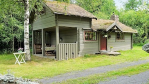 A rustic cabin with a porch, a small attached shed, and a thatched roof. - 5 Person Holiday Home in Tingsryd (Tingsryd)