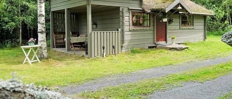 A rustic cabin with a porch, a small attached shed, and a thatched roof.