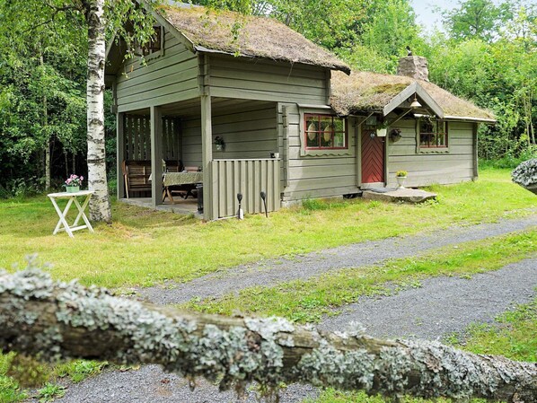 Une cabane rustique dotée d’une véranda, d’un petit abri attenant et d’un toit de chaume.