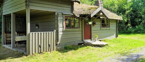 A rustic cabin with a porch, a small attached structure, and a thatched roof.