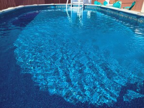 A clear swimming pool with a ladder leading into it, surrounded by a wooden fence and a few green chairs. - Holiday home with private heated pool available . for extra $20 for each night
 (Holiday)