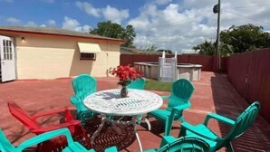 Une terrasse avec une table ronde et des chaises, un petit jardin et un bâtiment en arrière-plan.