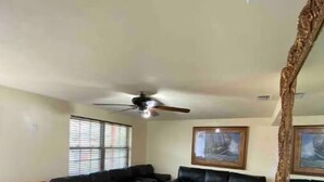 Un salon doté d’un ventilateur de plafond, d’un grand miroir et d’un canapé en cuir noir.