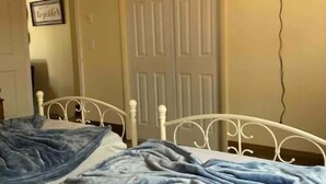Une chambre avec deux lits, un ventilateur de plafond, une porte et un téléviseur fixé au mur.
