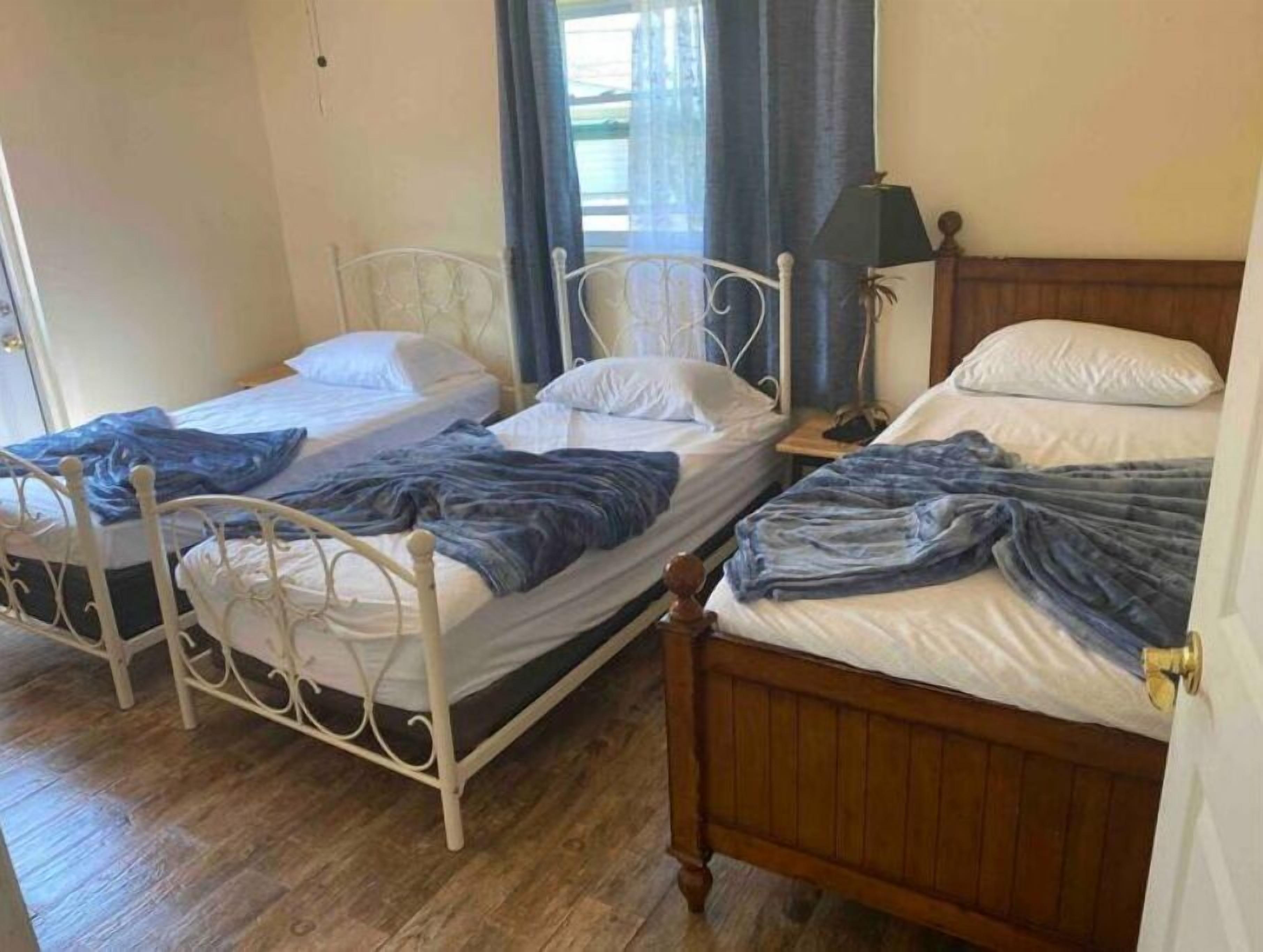 Ein Zimmer mit zwei Betten, eines mit weißem Metallgestell und das andere mit Holzgestell, beide mit weißer Bettwäsche und blauen Decken.
